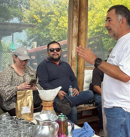 Visitantes escuchan una explicación sobre el café junto a una mesa con implementos de preparación.